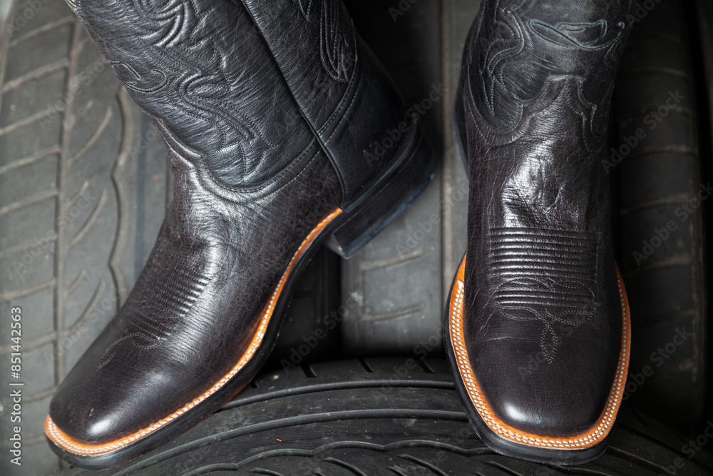 Male cowboy boots stand on car wheels.. Male cowboy boots stand on car wheels..