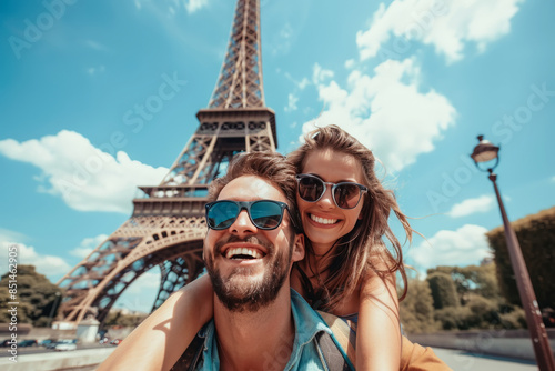 Pareja de jovenes llevando el hombre a la mujer a su espalda, sonrientes y alegres, haciéndose un selfie, sobre fondo de la torre Eiffel de la ciudad de París, en un bello día soleado de verano 