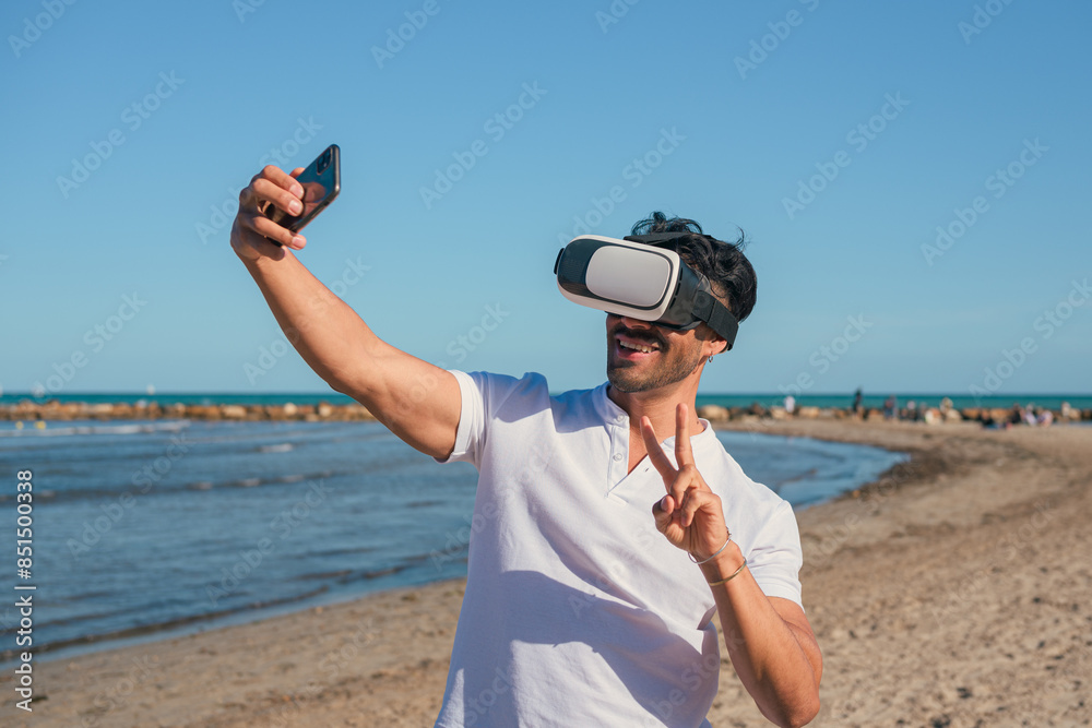 Obraz premium Man wearing virtual reality headset takes selfie on beach