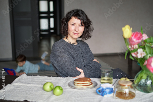 Fotografie Positive middle age women sitting the the table at home with tea and pancakes