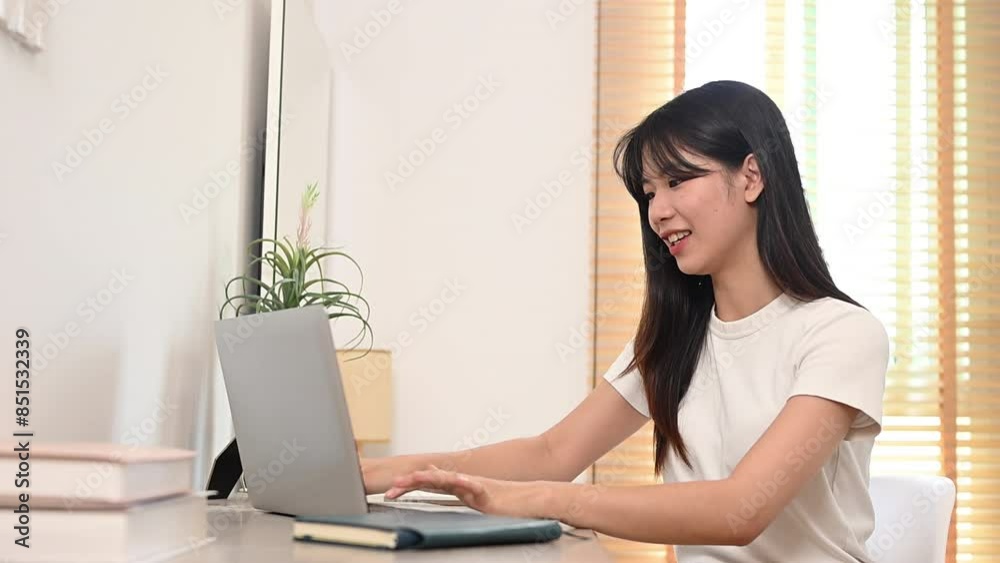 Pretty young Asian woman in casual clothing working online on laptop at home Pretty young Asian woman in casual clothing working online on laptop at home
