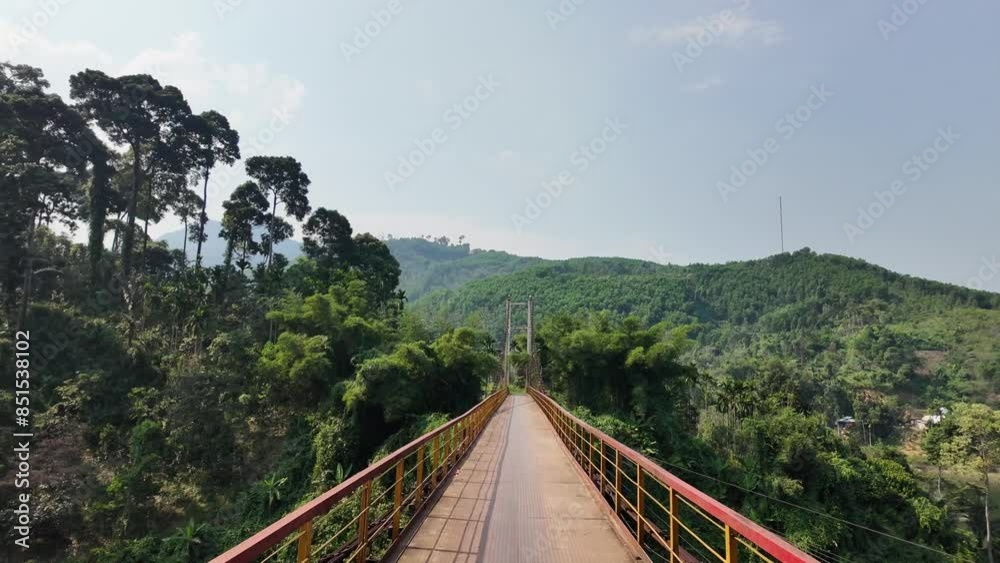 A serene suspension bridge stretches over a lush, green valley with towering trees under a clear summer sky, ideal for nature and adventure travel themes A serene suspension bridge stretches over a lush, green valley with towering trees under a clear summer sky, ideal for nature and adventure travel themes