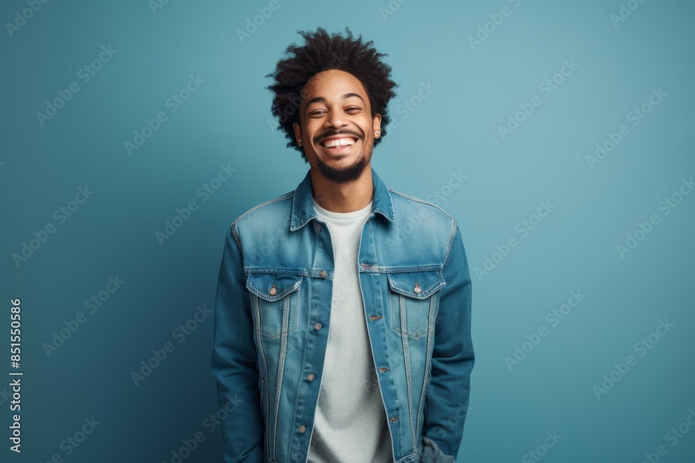 Fototapeta premium Portrait of a happy afro-american man in his 20s wearing a rugged jean vest while standing against blank studio backdrop