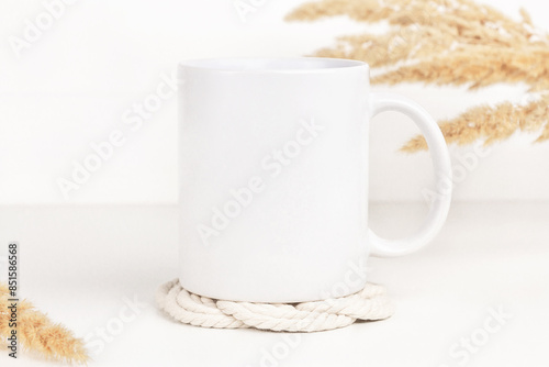 Mockup of white mug on table with coaster and dried flowers, neutral color. Blank coffee cup mug mock up in Boho style.