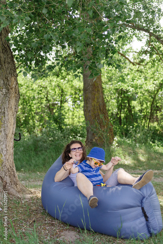 Mom and her child are playing on an inflatable couch under a tree in nature in the spring.