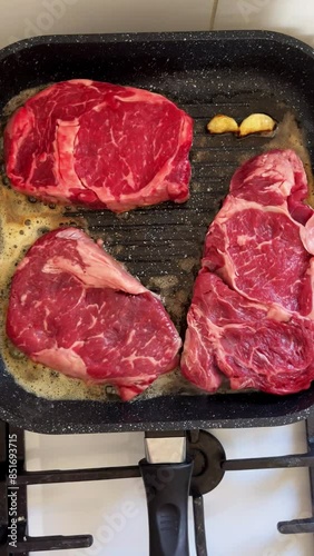 Three marbled beef steaks are fried in a frying pan on the stove in the kitchen.