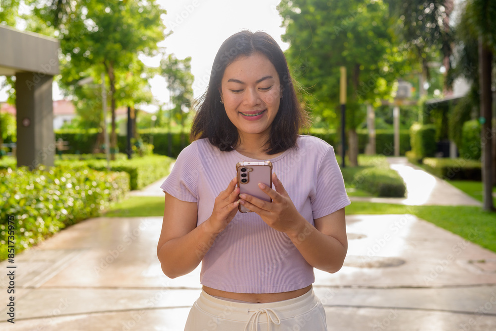 Fototapeta premium Portrait of beautiful Asian woman outdoor in park during summer using mobile phone
