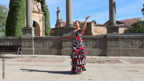 Video of woman dressed in typical Spanish flamenco costume dancing in a square to slow camera
