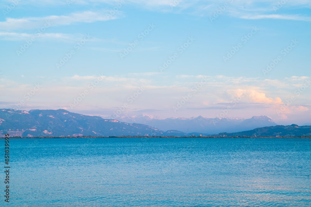 Germany, Beautiful sunset light shining on alps mountain chain behind water of bodensee in summer with snow covered peaks