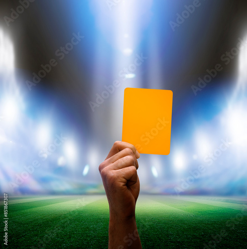 Hand mit gelber Karte in einer Fussballarena im Scheinwerferlicht