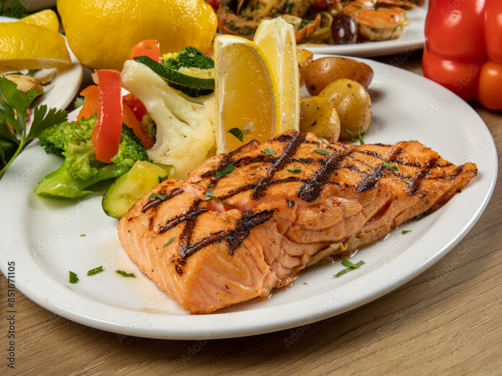 a dinner plate filled with a portion of grilled salmon filet and assorted vegetables in a restaurant setting a dinner plate filled with a portion of grilled salmon filet and assorted vegetables in a restaurant setting