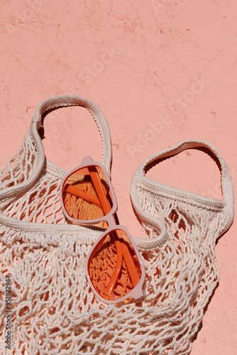 Orange sunglasses with mesh market tote on coral textured background in direct sunlight