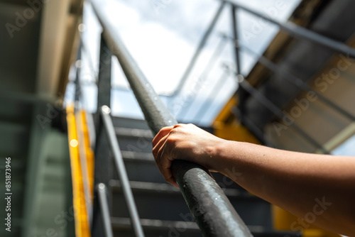 A human hand is holding the handrail banister during walking up the stairway at the factory workplace. People action scene, close-up and selective focus.