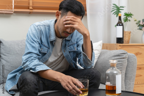 melancholy young Asian man drinks alcoholic whisky alone at home feeling dizzy after drunk