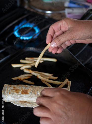 Concept of taking or grabbing food with hands, feminine mature Mexican hands. A burrito with french fryes over a comal using a stove with fire or flame in the background, vertical image photo