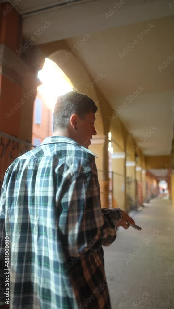 A young man walks through a vibrant archway corridor while using his smartphone A young man walks through a vibrant archway corridor while using his smartphone