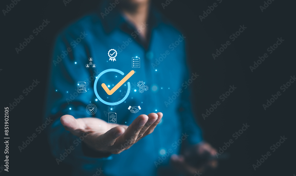 © Supatman - Businessman holding a digital icon of a checkmark with quality assurance and certification symbols, standard compliance and guarantee. quality control, automation process, Standardization management,
