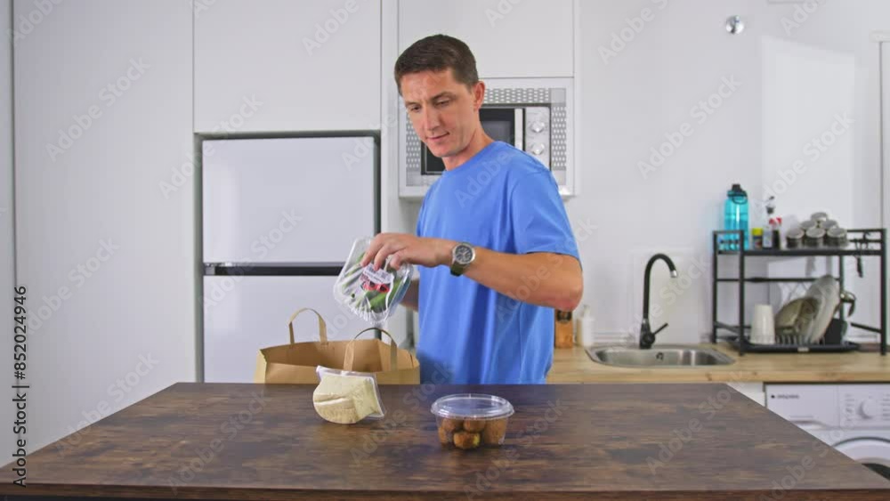 A man in a blue shirt unpacks groceries on kitchen counter, preparing a meal with fresh ingredients A man in a blue shirt unpacks groceries on kitchen counter, preparing a meal with fresh ingredients