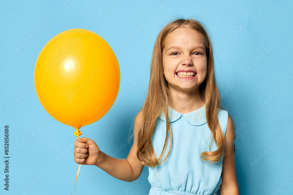 Joyful little girl holding a bright yellow balloon against a vibrant blue background Joyful little girl holding a bright yellow balloon against a vibrant blue background