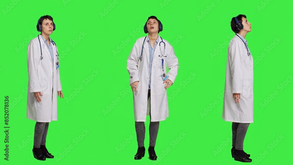 Joyful physician dancing around in the studio with music on headset, having fun with modern cool songs against greenscreen backdrop. Medic woman enjoying audio tunes and singing. Camera A. Joyful physician dancing around in the studio with music on headset, having fun with modern cool songs against greenscreen backdrop. Medic woman enjoying audio tunes and singing. Camera A.