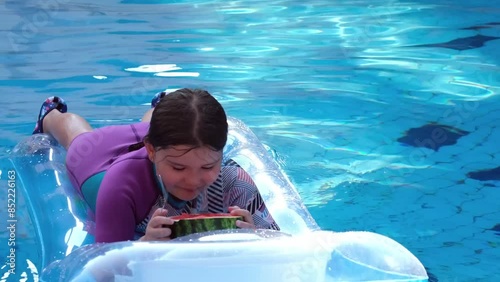 Child swim on a mattress in the pool and eat watermelon in the water. 