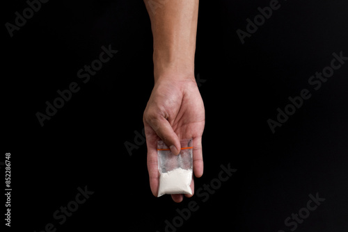 Hand giving cocaine in plastic package isolated on black background. Illustration of illegal drug substances, narcotics photo