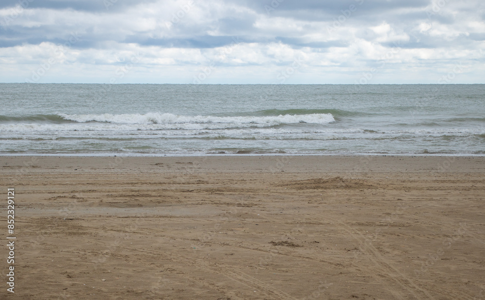 A photo of the sandy shore at Adriatic Sea in Rimini, with some waves in front and a cloudy sky A photo of the sandy shore at Adriatic Sea in Rimini, with some waves in front and a cloudy sky