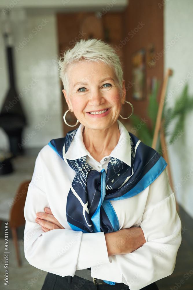 Fototapeta premium Portrait of confident happy successful senior businesswoman in elegant white blouse and silk scarf around neck standing with crossed hands and cheerful smile motivating you to run your own business