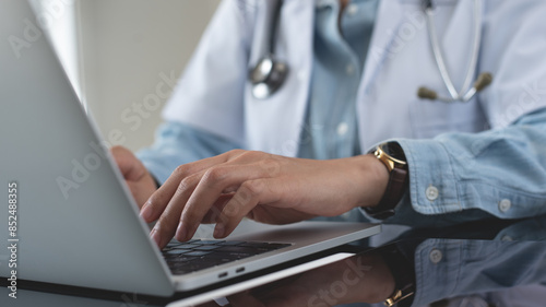 Female doctor working on laptop computer at doctor's office. writing prescripstion, recording patient's information, healthcare and medicine concept