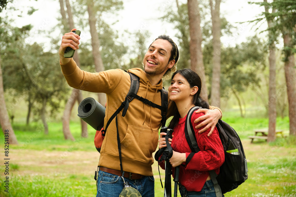 A man and woman hikers are taking a selfie in a park. They are carrying backpacks. Scene is happy and carefree A man and woman hikers are taking a selfie in a park. They are carrying backpacks. Scene is happy and carefree