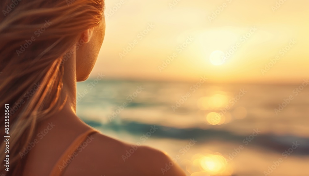 Serene woman enjoys stunning sunset at the beach with flowing hair and soft golden light reflecting off the ocean waves.