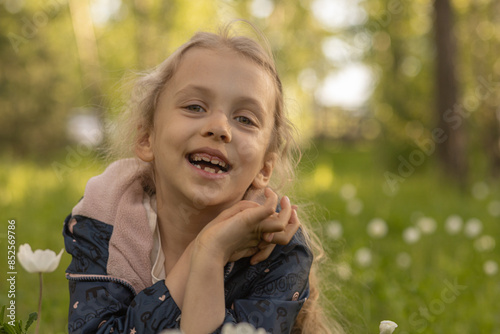A laughing girl with a gap-toothed smile. A little smiling girl on the flowery meadow in spring or summer. Exploring nature, real person