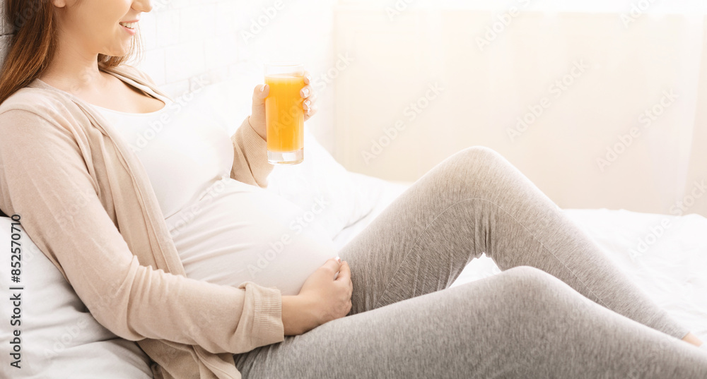 A pregnant woman is shown holding a glass of orange juice in her hand ...