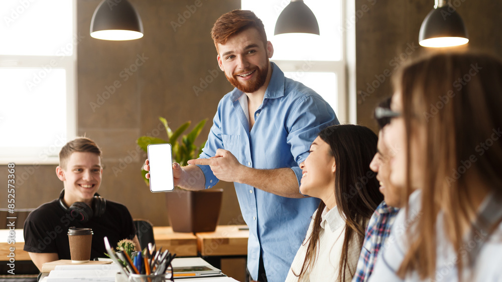 Fototapeta premium Student guy showing phone with blank screen to classmates, studying together in library