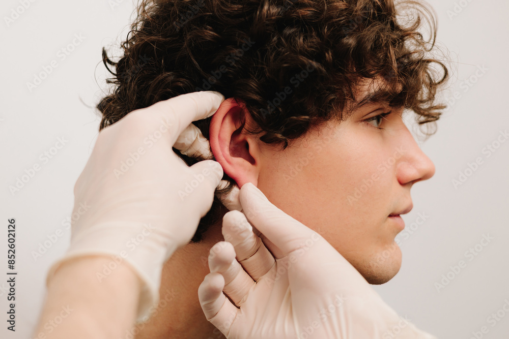 Fototapeta premium Process of examination patient before otoplasty surgery. Surgeon doctor makes palpation before cosmetic ear surgery.