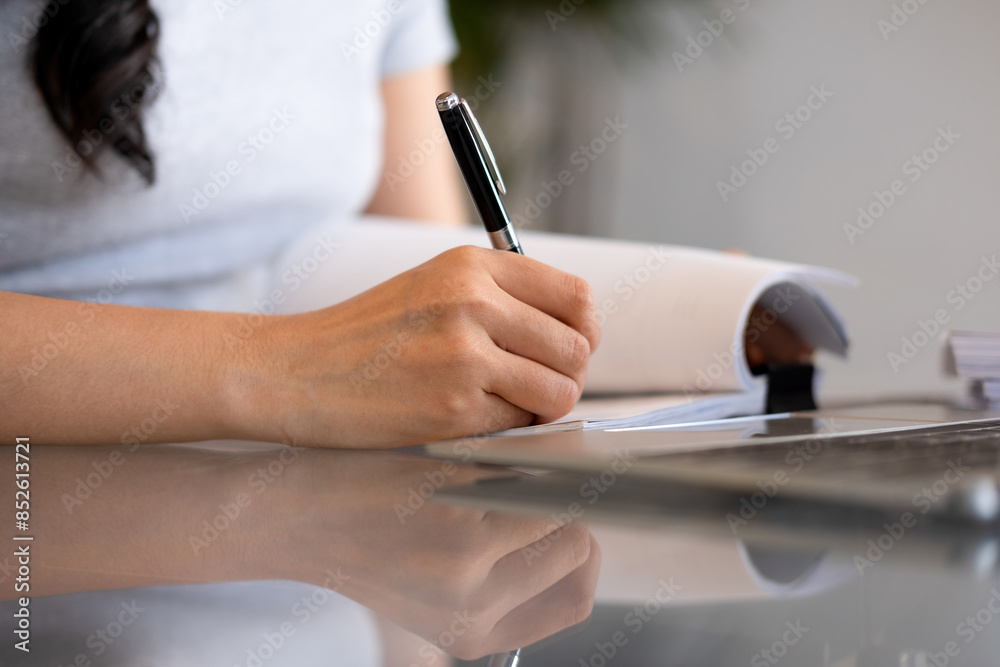 Fototapeta premium Young woman engages in note-taking at workspace.
