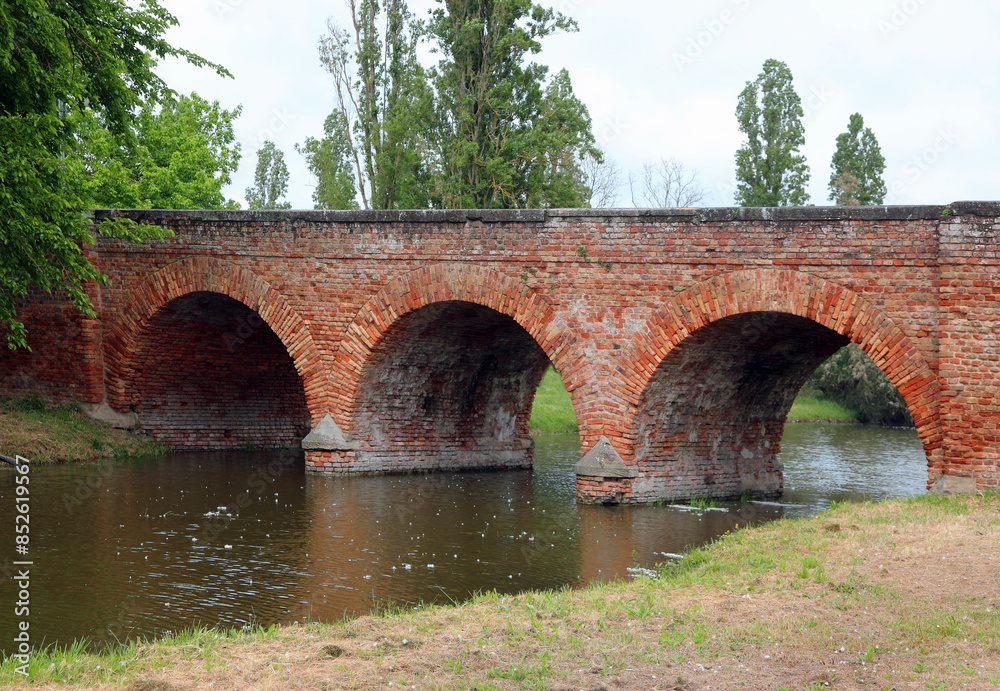 Fototapeta premium medieval bridge made of red bricks with three perfect arches over a canal with water