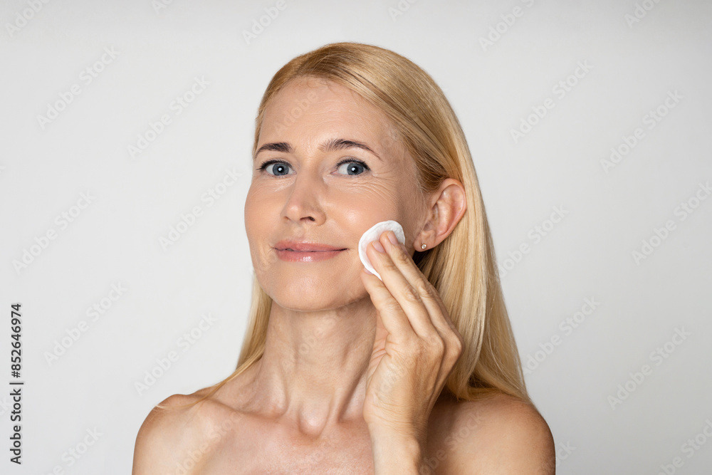A close-up portrait of a woman with blonde hair, wearing a white cotton pad to her face. She is looking directly at the camera and has a slight smile on her face. The background is plain white A close-up portrait of a woman with blonde hair, wearing a white cotton pad to her face. She is looking directly at the camera and has a slight smile on her face. The background is plain white