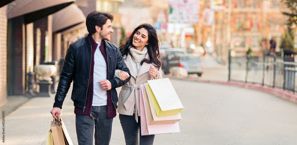 A man and a woman are strolling down a city street carrying shopping bags. A man and a woman are strolling down a city street carrying shopping bags.