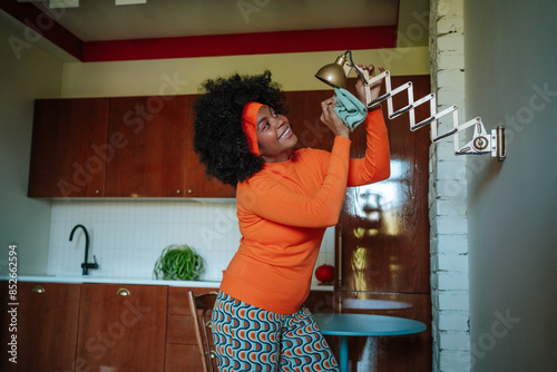 Woman in retro kitchen balancing a lamp humorously