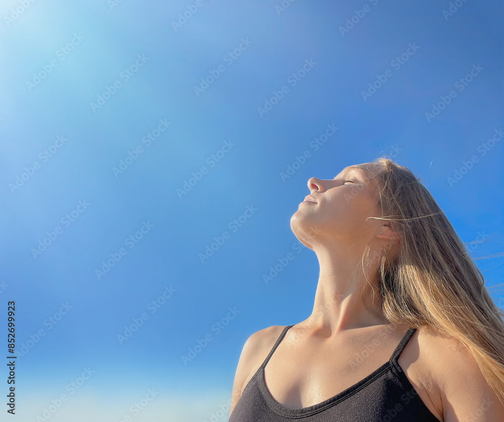 Portrait of a young relaxed girl, with long, light, loose hair, against a clear blue sunny sky, head turned to the rays of the sun, eyes closed. Sunbathing in the sun. Relaxes. Meditating. Portrait of a young relaxed girl, with long, light, loose hair, against a clear blue sunny sky, head turned to the rays of the sun, eyes closed. Sunbathing in the sun. Relaxes. Meditating.