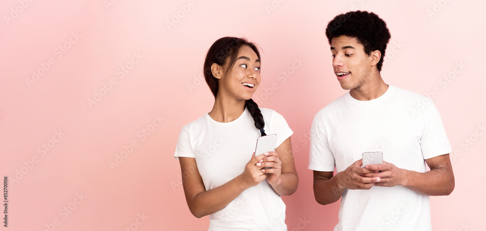 African American teenagers are standing together against a bright pink background. They are focused on a cell phone screen, appearing engaged with the content displayed, copy space African American teenagers are standing together against a bright pink background. They are focused on a cell phone screen, appearing engaged with the content displayed, copy space