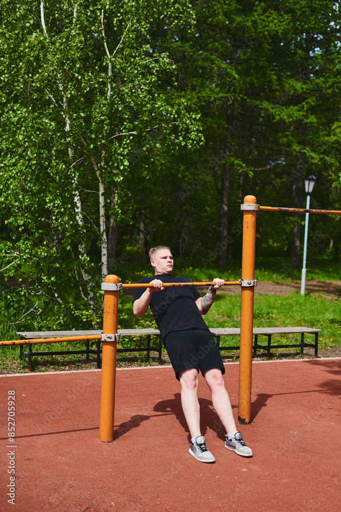 Obraz premium Caucasian male athlete doing pull-ups on the horizontal bar outdoors in a summer park