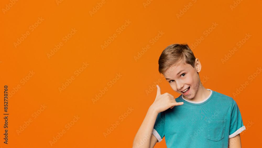 Communication concept. Flirty boy making call me gesture, smiling at camera, orange background with free space Communication concept. Flirty boy making call me gesture, smiling at camera, orange background with free space