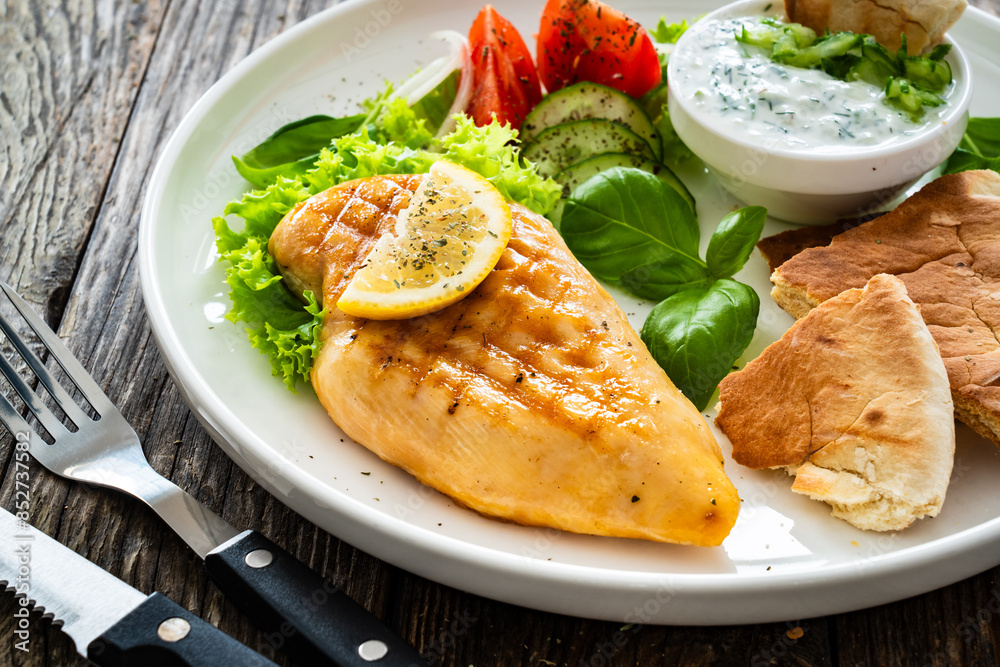 Seared chicken breast, pita bread and tzatziki on wooden table Seared chicken breast, pita bread and tzatziki on wooden table