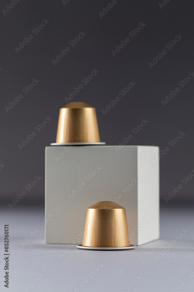 Two coffee capsules displayed on a white cube against a dark gradient background