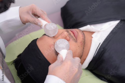 Close-up of a man undergoing a facial massage using cooling ice globes at a spa. Relaxation and skincare treatment concept. photo