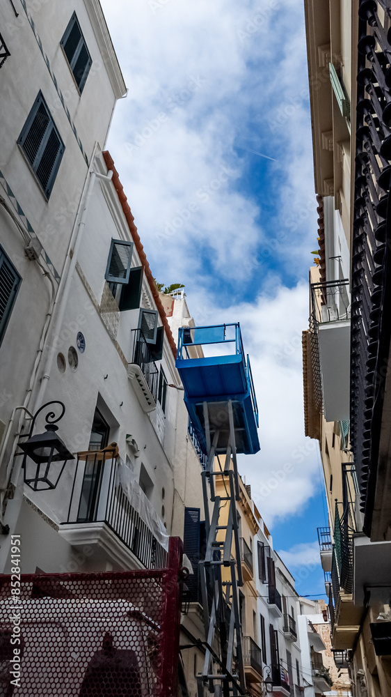 Naklejka premium Narrow European alley with traditional white buildings and a vivid blue balcony under a clear sky, ideal for travel and architecture themes