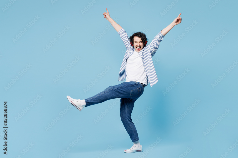 Full body young happy man wear shirt white t-shirt casual clothes listen to music in headphones raise up hands dance isolated on plain pastel light blue background studio portrait Lifestyle concept. Full body young happy man wear shirt white t-shirt casual clothes listen to music in headphones raise up hands dance isolated on plain pastel light blue background studio portrait Lifestyle concept.