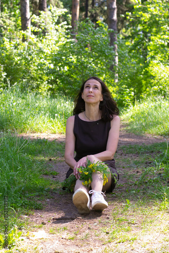 Woman sitting in forest with bouquet of flowers